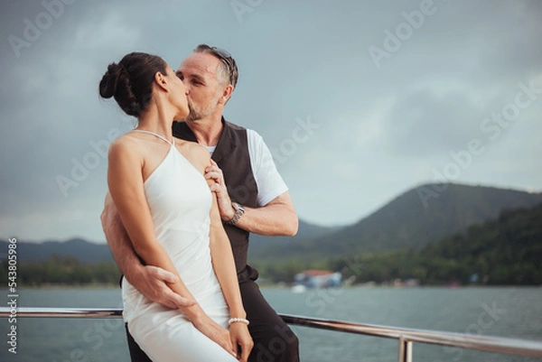 Fototapeta Romantic couple love hugging and kissing on yacht. Happy man and woman standing and hugging in cruise ship while sunset on vacation. luxury and honeymoon lifestyle, Happy aniversary.
