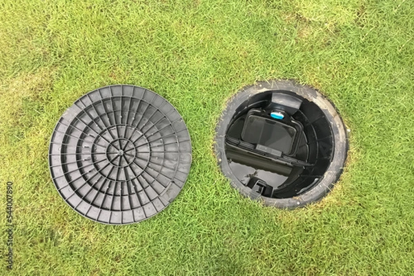 Fototapeta Image of a septic tank grease trap for home use to help collect light liquids such as fats, oils, and grease from the kitchen buried underground with green grass cover.