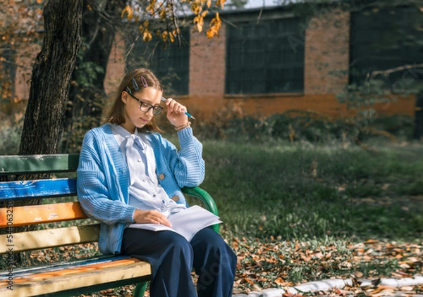 Fototapeta A teenager on a bench is doing homework on a sunny autumn day.