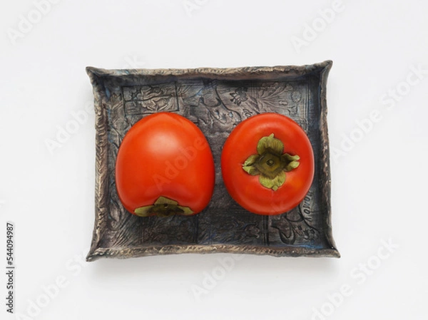 Obraz Persimmon fruits on a blue ceramic plate on a white background. Top view. Directly above photo.