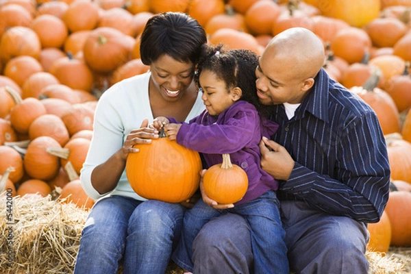 Obraz Happy family sitting on hay bales and holding pumpkins.