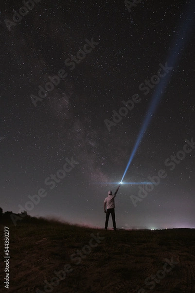 Fototapeta Beautiful night sky with stars and silhouette of a standing alone man on the mountain with a lantern. Blue milky way and man on the hill. Background with galaxy and silhouette of a man. 