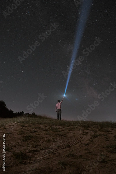 Fototapeta Beautiful night sky with stars and silhouette of a standing alone man on the mountain with a lantern. Blue milky way and man on the hill. Background with galaxy and silhouette of a man. 