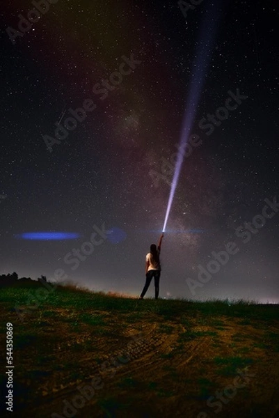 Fototapeta Beautiful night sky with stars and silhouette of a standing alone woman on the mountain with a lantern. Blue milky way and man on the hill. Background with galaxy and silhouette of a man. 