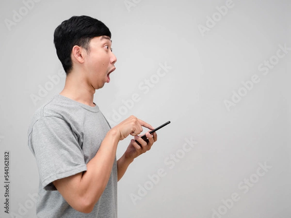 Fototapeta Man grey shirt feels shocked gesture press smart phone in his hand side view isolated