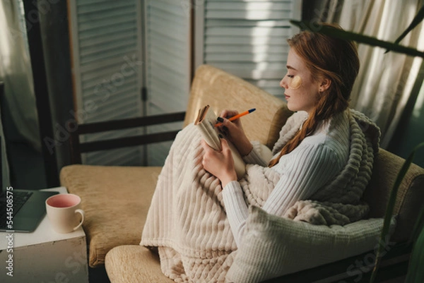 Fototapeta Cute lady with eyes patches at home writing notes on a diary while relaxing taking a break, enjoying home lifestyle. Resting, vacation, beauty treatment