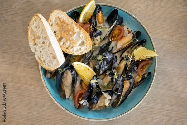 Fototapeta Cooked baked mussels in sauce with lemon and croutons on a blue plate top view