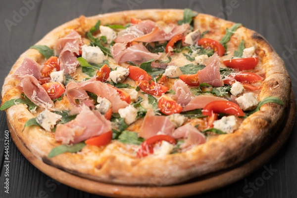 Fototapeta Pizza with prosciutto, arugula and parmesan on wooden background, top view. Italian cuisine.