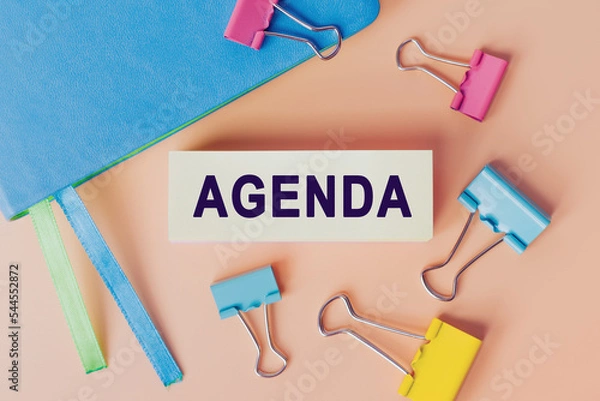 Fototapeta Text AGENDA written on white paper. Note near notebook and many colourful paper clips, top view. Business concept. Home Office