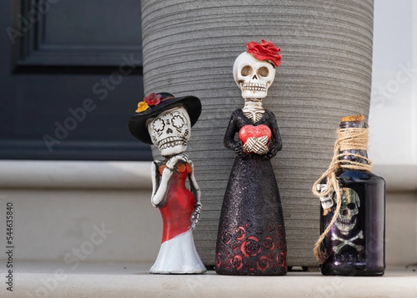 Fototapeta Halloween decoration elements: Mexican style skeleton statuettes and pirate bottle. On a house doorstep. 