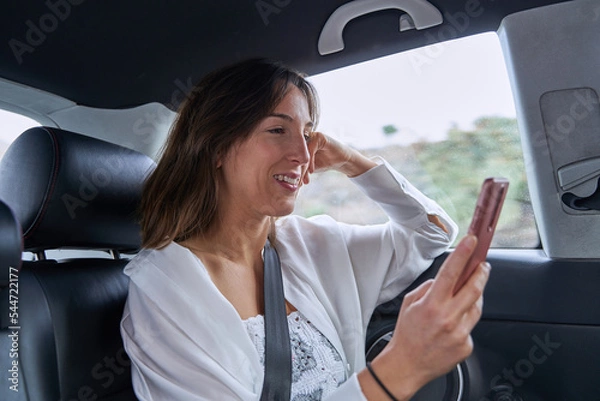 Obraz pretty girl surfs the internet with her mobile while smiling inside a car