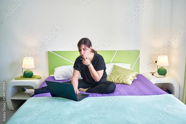 Fototapeta Caucasian pensive woman with focused face looking at computer from bedroom