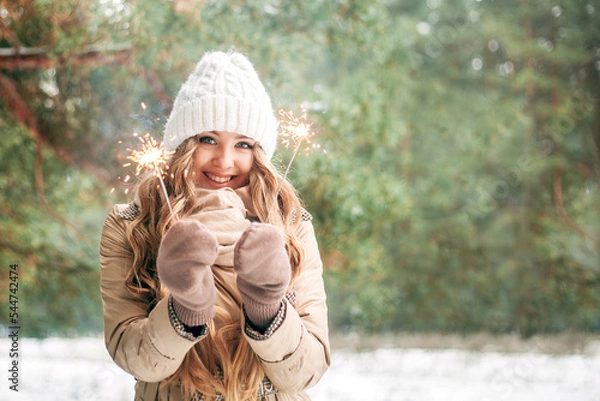 Fototapeta Beautiful sweet girl holds sparklers in her hands. Girl is blonde against the background of the winter forest. Concept of the holiday - New Year, Christmas, St. Nicholas Day. Banner. Place for text.