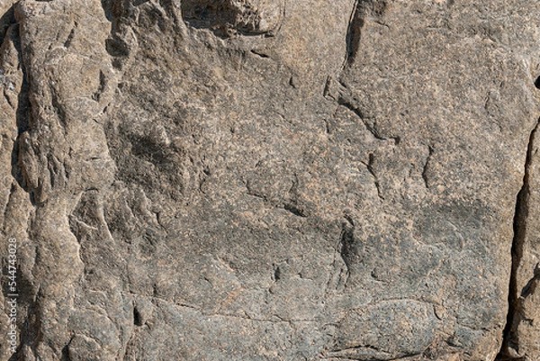 Fototapeta Textural stone background is gray with dark patterns and spots. Stone wall is gray with uneven bulges and cracks.