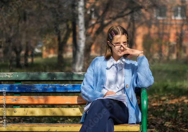 Fototapeta A teenager on a bench is doing homework on a sunny autumn day.