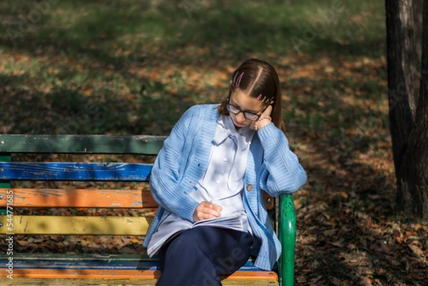 Fototapeta A teenager on a bench is doing homework on a sunny autumn day.