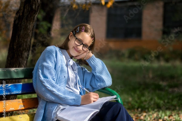 Fototapeta A teenager on a bench is doing homework on a sunny autumn day.