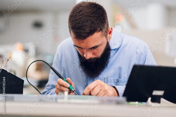 Fototapeta Electronics engineer working in a workshop with tin soldering parts