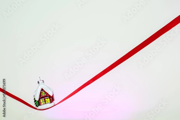 Fototapeta Minimalistic Christmas card. Christmas tree toy winter house on a red ribbon. Happy New Year 2023. Merry Christmas greetings.