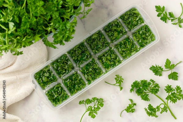 Fototapeta Frozen herbs for cooking. Fresh organic parsley and parsley ice cubes on a marble background. The concept of frozen food. Selective focus, top view and copy space