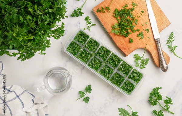 Fototapeta Frozen herbs for cooking. Fresh organic parsley and parsley ice cubes on a marble background. The concept of frozen food. Selective focus, top view and copy space