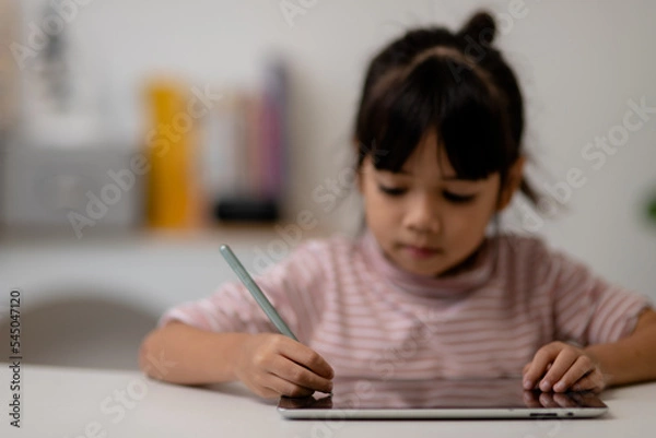 Fototapeta Asian little cute girl touching the digital tablet screen on the table