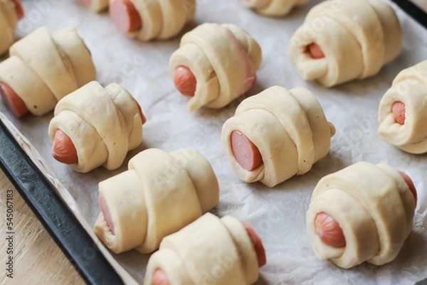 Fototapeta rolled dough blanks for croissants with sausages on a baking sheet before baking selective focus
