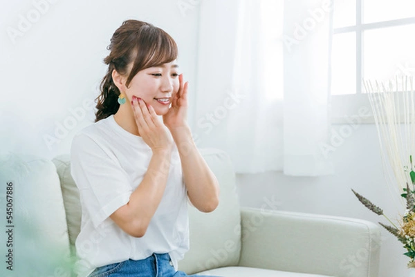 Fototapeta ソファに座りながらスキンケアのホームケアをする日本人女性
