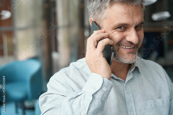 Fototapeta Gray-haired middle-aged man in stylish shirt is talking on mobile phone