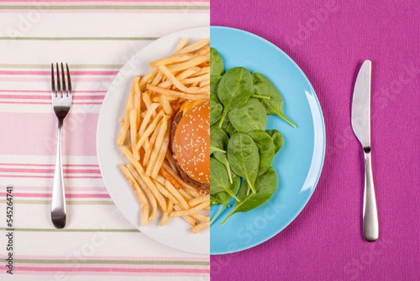 Fototapeta burger with french fries and fork on one side of the dividing line and baby spinach leaves and knife on another half. flat lay diet concept image of healthy and unhealthy eating