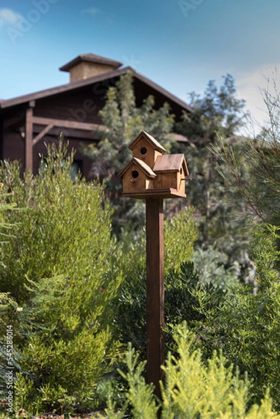 Obraz Handmade triple birdhouse on a wooden tall stand against a blurred cottage.
