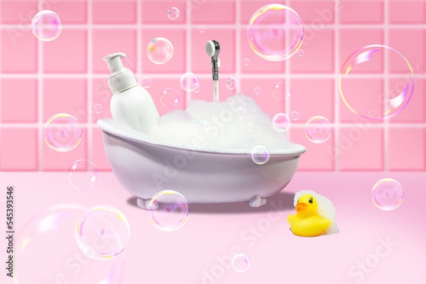 Fototapeta White bath with foam and soap bubbles, with a yellow duck and a bottle of cosmetic product on a pink background. Concept photo.