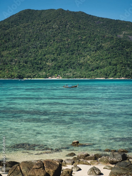 Fototapeta Scenic view of Sunset Beach, Koh Lipe Island. Small local long tail boat on crystal clear turquoise sea with coral reef transparent shallow water against Koh Adang Island background. Satun, Thailand.