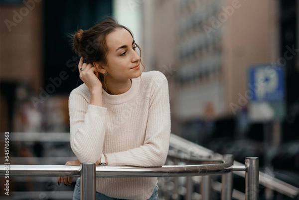 Fototapeta Professional woman worker wear standing outdoor terrace with a smile leaning on railing enjoy view from modern office skyscraper. Tall stylish girl near the railing and steps on the city background.