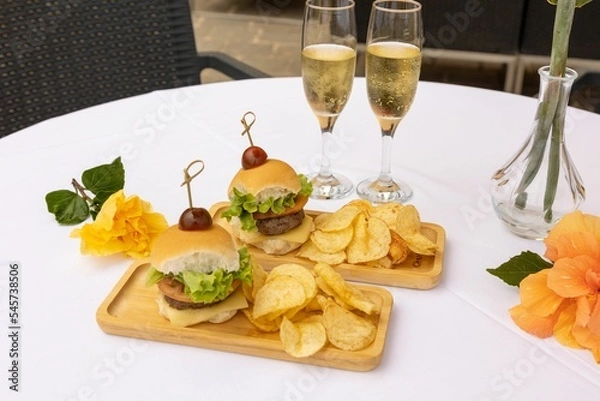 Fototapeta Top closeup of burger and chips on the wooden plates, two glasses full of champagne