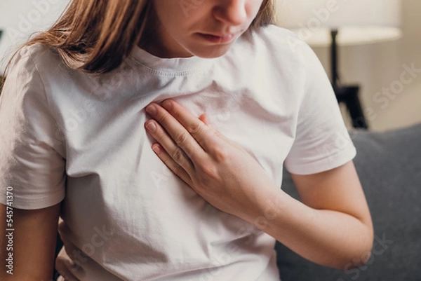 Obraz Young unhealthy female sit on couch having difficulty breathing pain of heart, touches his chest with hand. Trouble breathing, chest pain. Heart attack, thoracic osteochondrosis, panic attack concept