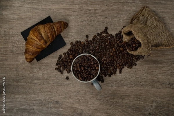 Obraz Top view of brown roasted coffee beans spilled on a table with a full coffee mug and biscuit