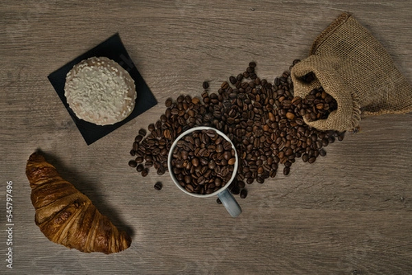 Obraz Top view of brown roasted coffee beans spilled on a table with a full coffee mug and biscuit