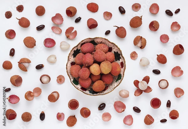 Obraz Lychee fruits in bowl on white background with scattered whole and peeled fruit, with seeds and peels. Top view. Decorative arranged lychees in flat lay style.