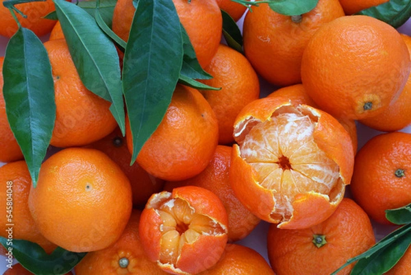 Obraz Mandarin oranges fruit with a decoratively peeled piece and with fresh leaves. Detailed top view. Close up photo.