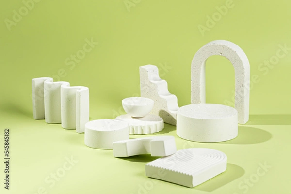 Fototapeta An empty stage with a composition of white podiums of different sizes and shapes on a green background and shadows