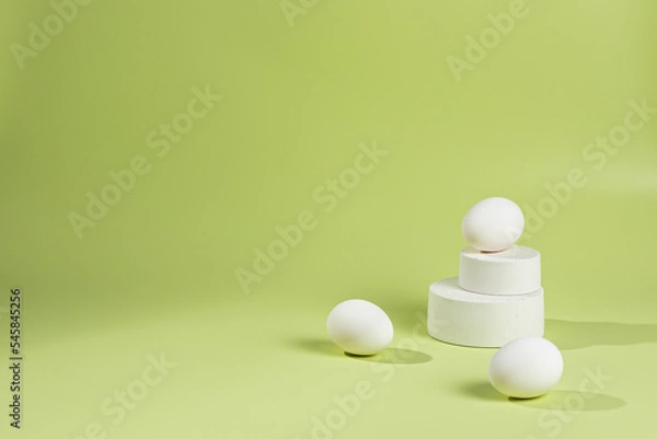 Fototapeta Eggs lie on a pyramid of white podiums on a green background with a shadow from sunlight