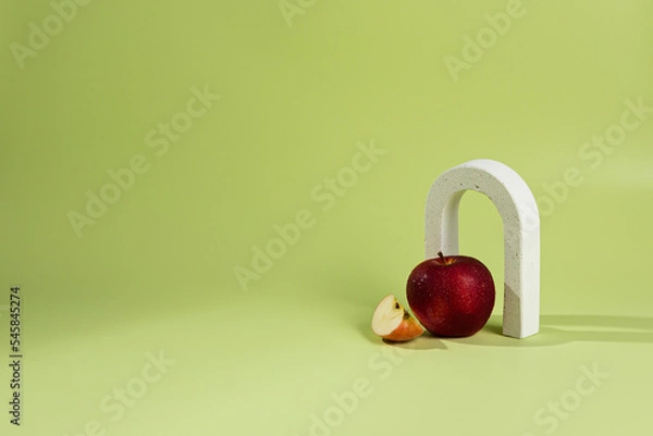 Fototapeta An empty stage with one white concrete arch under it a red apple. On a green background and a shadow from sunlight