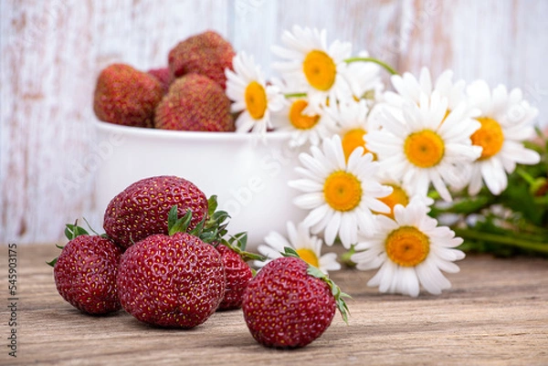 Fototapeta Large ripe strawberries on the background of a plate with berries and a bouquet of daisies. Macro photography