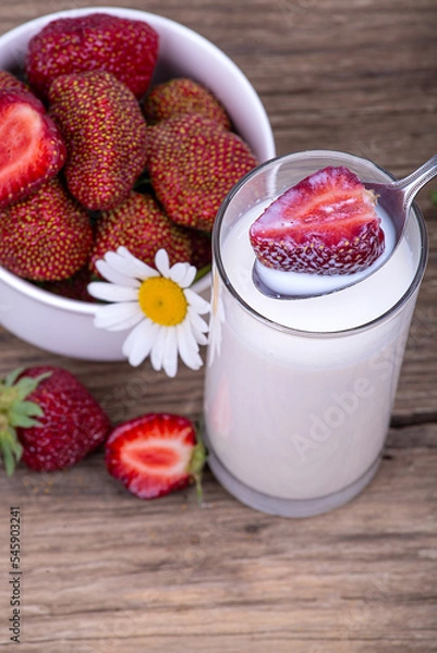 Fototapeta Ripe strawberries in milk, a plate with strawberries on a wooden background, close-up
