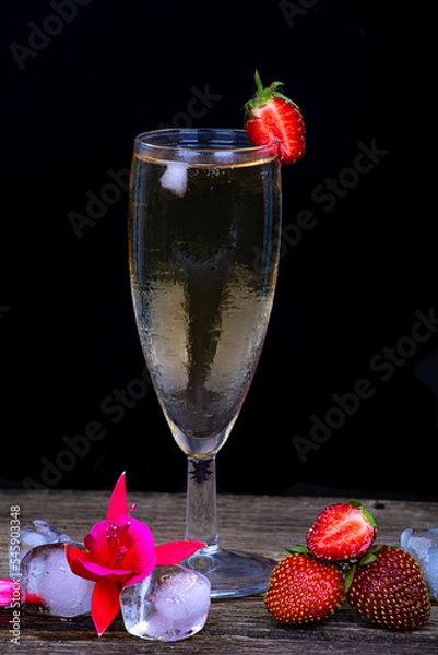Fototapeta A misted glass of champagne, fresh strawberries and pieces of ice on a dark background