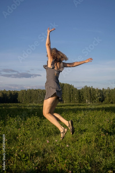 Fototapeta a woman jumps in flight hands in different directions in a summer field in a black sundress