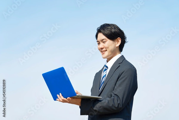 Fototapeta 外でノートパソコンを使うビジネスマン　青空背景
