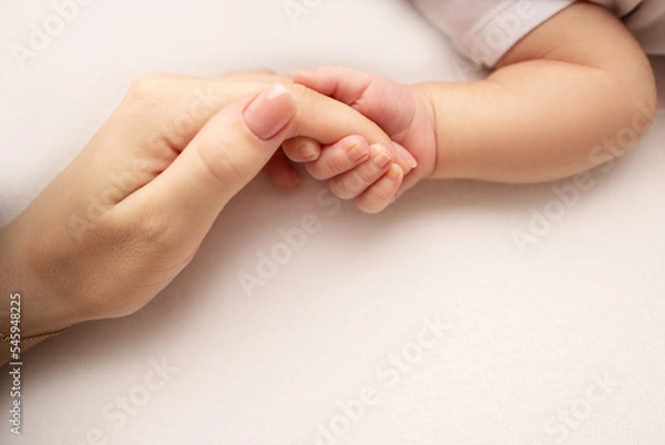 Fototapeta Close-up little hand of child and palm of mother and father. The newborn baby has a firm grip on the parent's finger after birth. A newborn holds on to mom's, dad's finger. 