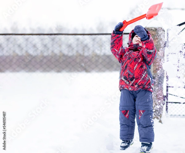 Fototapeta Little boy playing with a red shovel in the snow. Winter activity